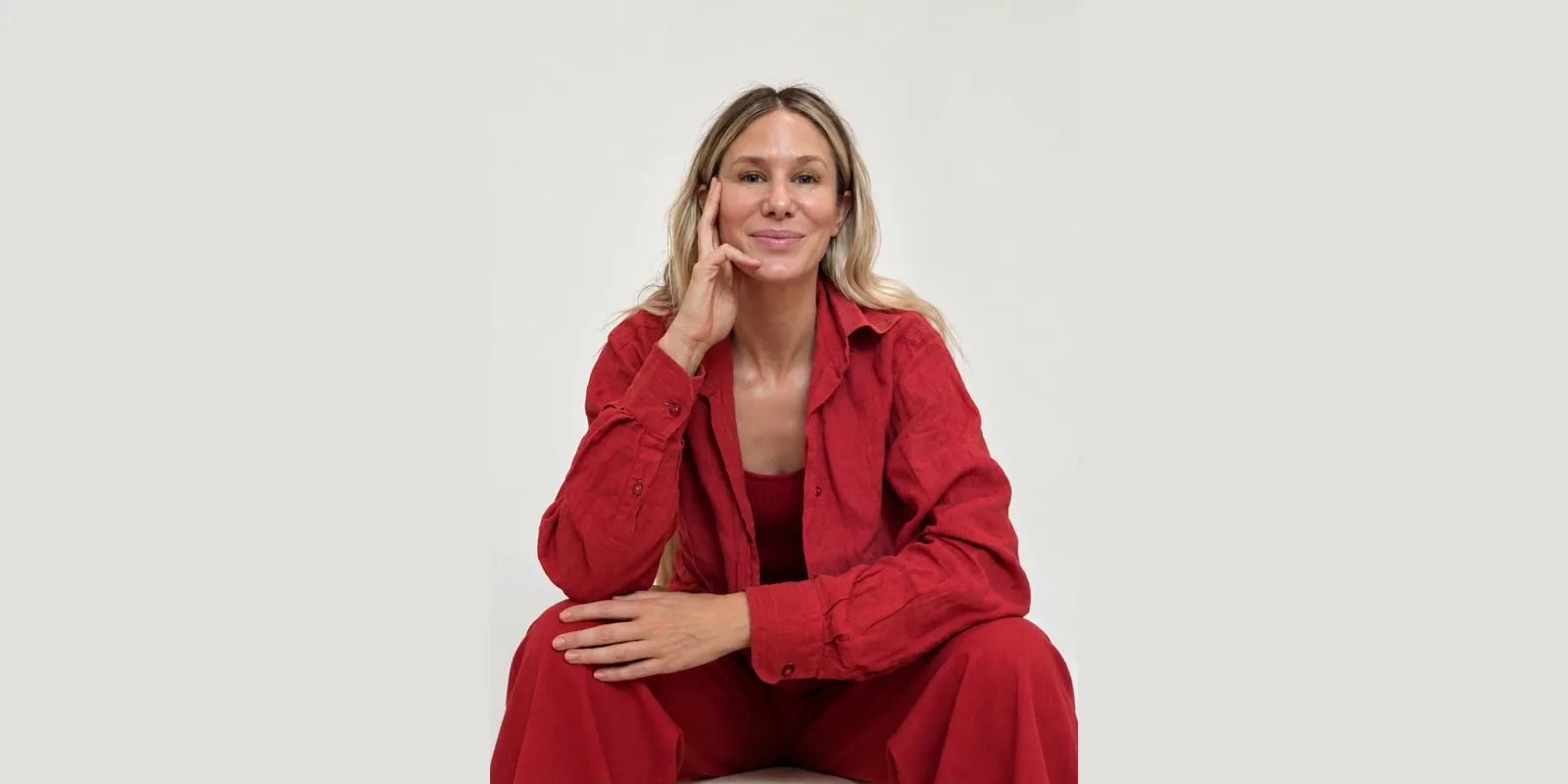 Dr Sophie Mort in a red outfit, sitting and smiling, hand resting on her cheek